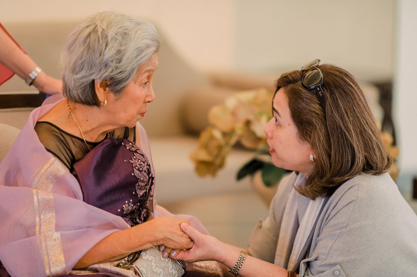 An adult daughter holding her elderly mother’s hands while they talk