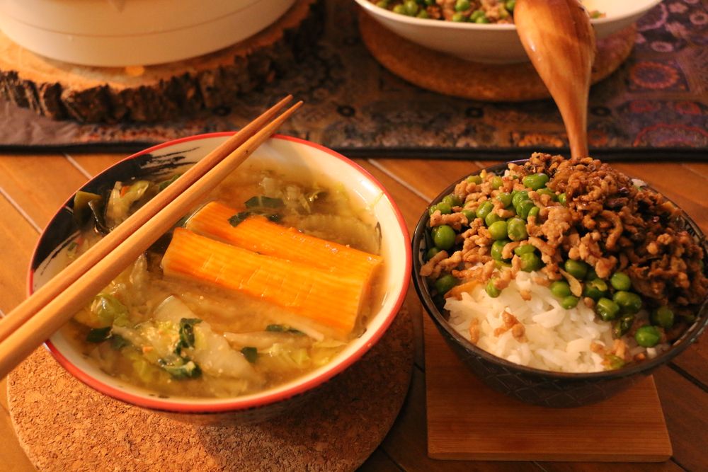A bowl of vegetable soup next to a bowl of rice with minced meat and peas